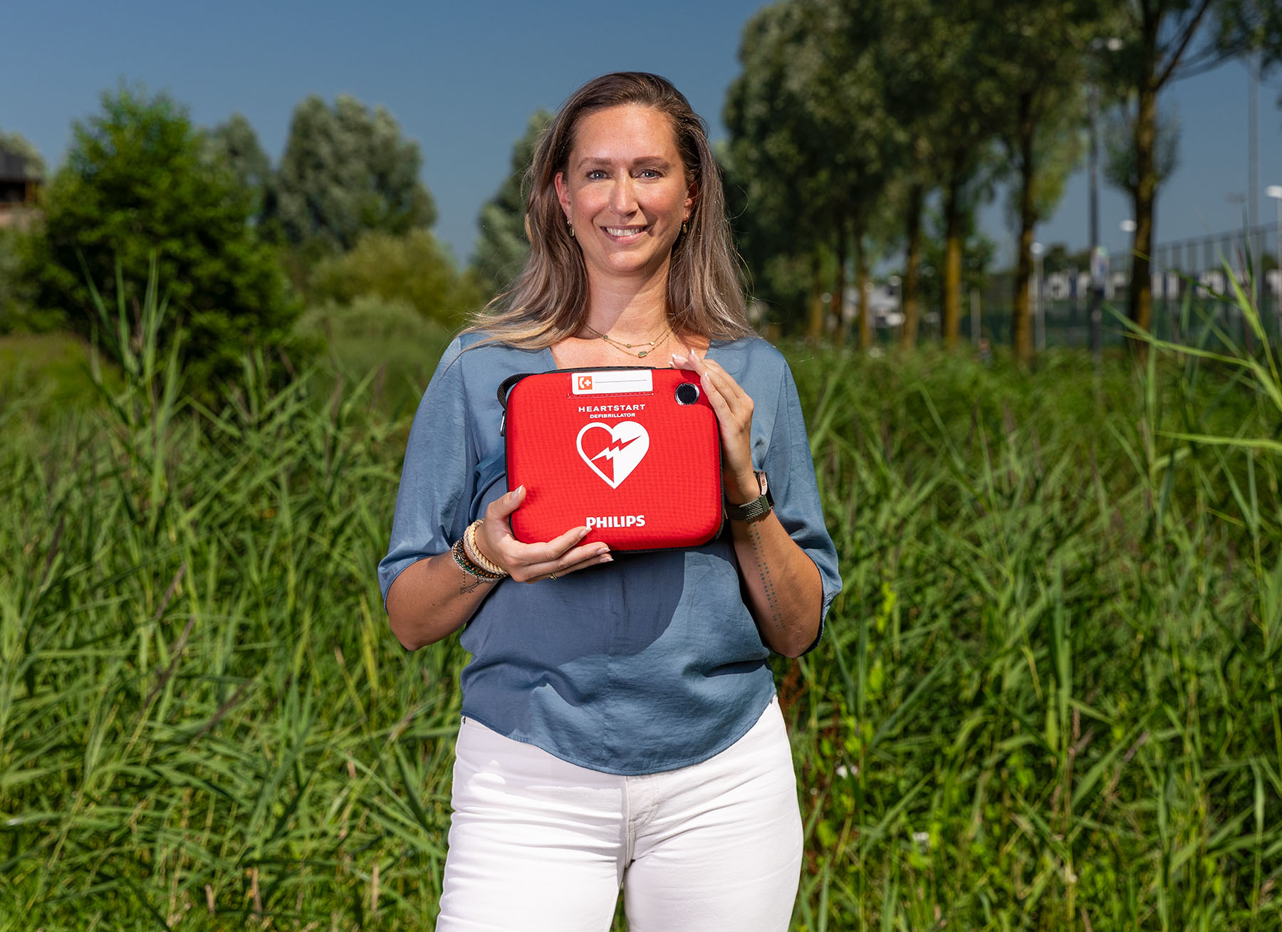 Vrouw houdt een rode Philips AED vast in een groene buitenomgeving